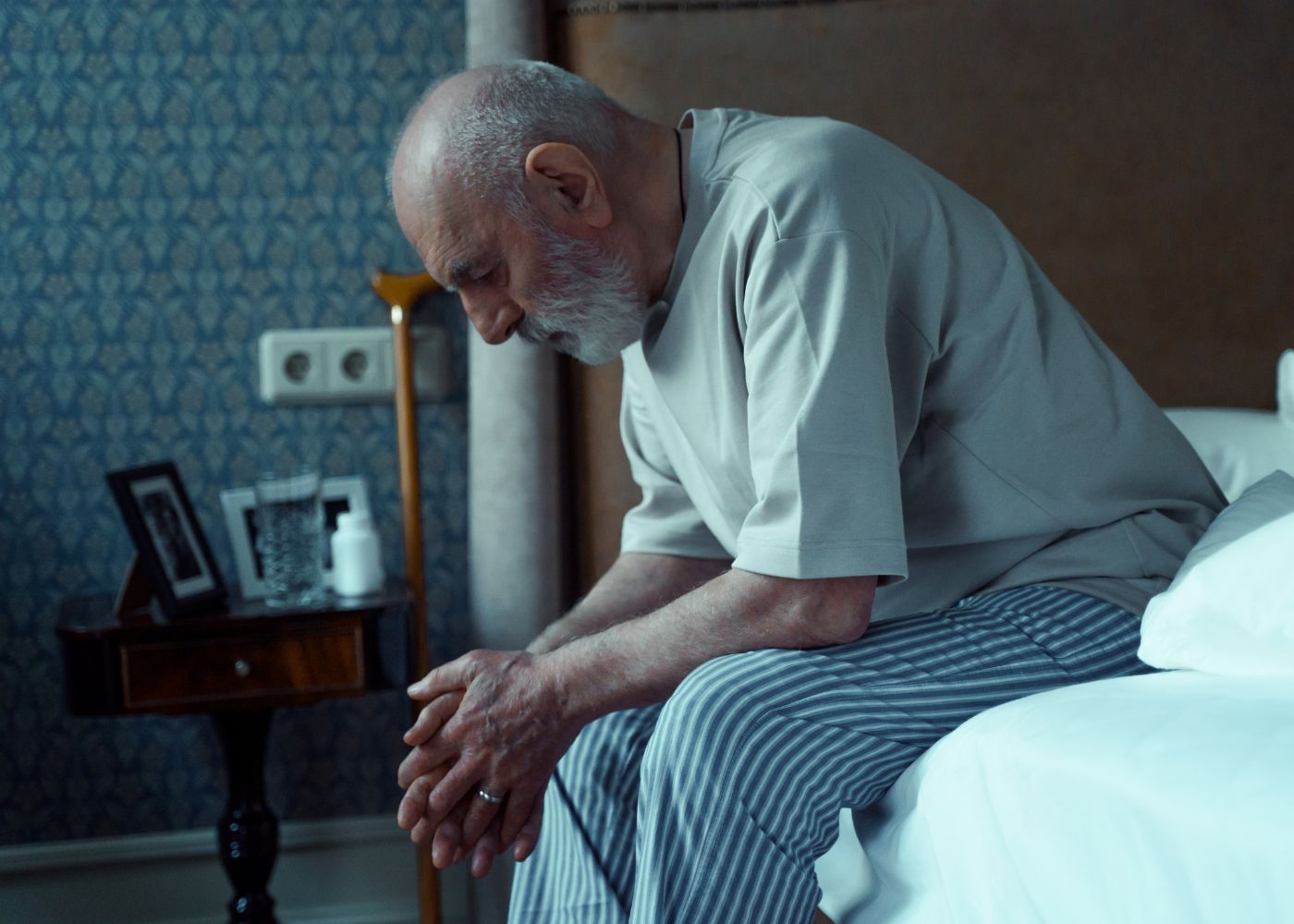alter Mann sitzt auf Bett